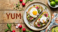 Avocado toast with fried egg, radish slices, and microgreens on rustic wooden table with YUM spelled in spices, top view.