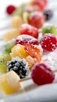 Fresh fruit skewers with powdered sugar dusting, featuring colorful berries, kiwi, and tropical fruits arranged on white plate for catering and dessert presentations.