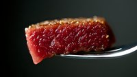 Juicy piece of rare tuna steak on fork against dark background, close up macro shot showing meat texture and pink color gradient. Fresh seafood cuisine.