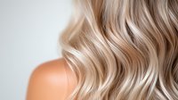 Luxurious blonde wavy hair with soft highlights and natural texture on light background, close-up view of professional hairstyling and coloring result.