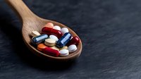 Colorful pharmaceutical pills and capsules on wooden spoon against dark background, medical concept for healthcare, medicine, and supplements.