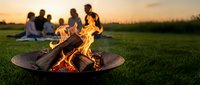 Friends gathering around outdoor fire pit during golden hour sunset creating warm social atmosphere for backyard entertainment and relaxation.