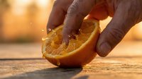 Hand holding fresh orange slice with juice dripping, golden sunlight background, food photography for culinary, beverage, and healthy eating content.