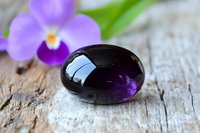 Purple amethyst gemstone with orchid flower on rustic wooden background for jewelry design, healing crystals, meditation and wellness concepts.