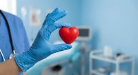 Healthcare professional in blue medical gloves holding red heart symbol in clinical setting representing cardiology care and cardiovascular health services.