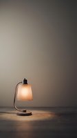 Minimalist desk lamp with frosted glass shade emitting warm light against neutral gray wall, creating ambient glow on wooden surface for interior design and home decor projects.