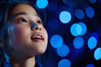 Young Asian woman looking up with wonder against blue bokeh lights background, capturing moment of joy and anticipation during night celebration.