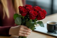 Fresh red roses bouquet held by woman in burgundy sweater with coffee cup on table, romantic lifestyle moment captured in soft natural light.