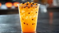 Fresh orange bubble tea with black tapioca pearls in plastic cup on dark background, selective focus on sweet cold Asian drink with boba balls.