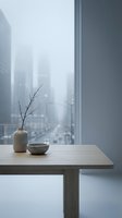 Minimalist wooden table with ceramic vase and bare branch near window overlooking foggy cityscape. Serene interior design for home decor, wellness, and lifestyle concepts.