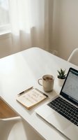 Minimalist home office workspace with laptop showing financial charts, coffee mug, notebook and small plant on white desk near window with natural light.