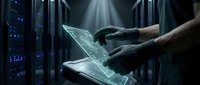 Technician in dark gloves holding holographic digital interface tablet in server room with illuminated data center equipment and network infrastructure visible in background.