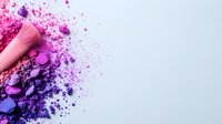Vibrant makeup brush with scattered pink and purple cosmetic powder creating artistic texture on light background. Professional beauty and cosmetics concept.