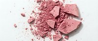 Crushed pink powder and broken makeup chunks scattered on white surface, suitable for cosmetics, beauty product advertising, and makeup tutorials.