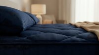 Cozy bedroom scene with navy blue quilted bedding, soft pillows, and warm natural light from window, perfect for home decor and lifestyle content.