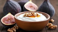 Fresh figs and creamy yogurt with honey and walnuts in ceramic bowl on rustic wooden table, healthy breakfast composition with natural ingredients.