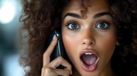 Young mixed race woman with curly hair expressing surprise while talking on mobile phone against blurred background, showing genuine emotional reaction.