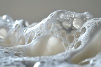 White soap foam with bubbles macro photography showing delicate texture and light patterns, abstract minimalist composition with soft focus and bokeh effect.