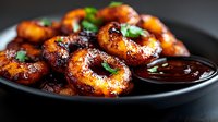 Glazed golden potato rings with caramelized coating and fresh herbs served on dark plate with dipping sauce for gourmet appetizer presentation.