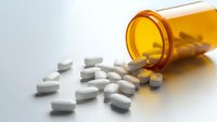 White prescription pills spilling from amber medicine bottle on clean surface for healthcare and pharmaceutical concepts.