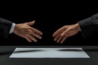 Business partners reaching hands across table with blank document, symbolizing deal negotiation, agreement, and professional collaboration on dark background.
