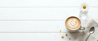 Overhead view of latte with latte art on white wooden surface, featuring daisy flower and spoon for café, coffee shop, and beverage marketing.
