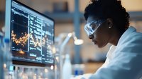 Young African American female scientist analyzing data on multiple screens in laboratory setting with protective eyewear and white coat.