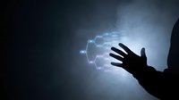 Silhouetted hand reaching toward glowing electric energy orb with blue and purple lightning effects against dark background for technology, power, innovation, and science concepts.