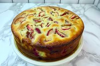 Homemade plum cake with golden crust and fresh fruit slices baked in rich batter on white marble surface for dessert recipes and baking content.