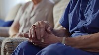 Elderly male hands clasped together in comfort during support group or counseling session with caregivers, representing compassion, healthcare assistance, and emotional wellbeing for seniors.