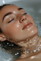 Young Asian woman with glowing wet skin relaxing in water with closed eyes, natural makeup and dewy complexion showing skincare and wellness concept.