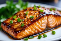 Grilled salmon fillet glazed with teriyaki sauce, garnished with sesame seeds and fresh chopped green onions served on white plate, close up view of seafood dish.