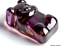 Purple gummy bear candy with translucent glossy surface catching light and creating shine effects, macro photography on white background showing sweet treat details.