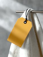 Yellow blank price tag hanging on white towel on metal rack with soft window light and shadows. Clean minimal composition for spa, hotel or retail concepts.