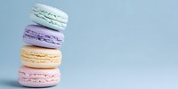 Stack of colorful French macarons in pastel colors - mint green, lavender, peach, and pink - against light blue background for food marketing.