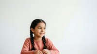 Young South Asian girl with long braided dark hair wearing a coral pink shirt, looking thoughtfully to the side against a white background. Suitable for educational, lifestyle, and children's content.