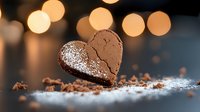 Heart shaped chocolate cookie dusted with powdered sugar on dark surface with golden bokeh lights and crumbs, romantic mood for Valentine's day celebration.