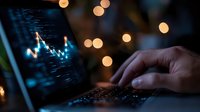 Trading chart with glowing blue line graph displayed on laptop screen in dark room with bokeh lights, hand typing on keyboard for financial analysis.