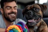 Happy Caucasian man with beard smiling at his brindle boxer dog with colorful rope toy in car, representing pet companionship and travel.