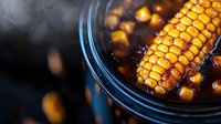 Grilled corn on the cob with charred kernels in cast iron skillet, smoky barbecue cooking with steam rising from hot surface for summer outdoor dining.