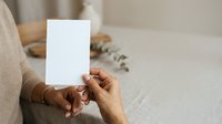 Hands holding blank white card mockup, woman wearing beige sweater displaying empty paper for greeting, invitation, or promotional message design.