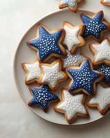 Star-shaped sugar cookies decorated with royal icing in navy blue and white colors with dotted patterns arranged on gray ceramic plate, festive holiday baking.
