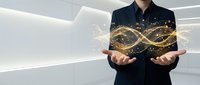Professional businessman in dark suit presenting glowing golden infinity symbol with sparkling particles in modern white office environment.
