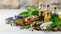 Natural essential oils in glass bottles with fresh herbs, spices and aromatherapy ingredients on wooden surface for wellness and holistic healing treatments.