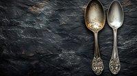 Two ornate vintage spoons with decorative handles on dark slate stone background for culinary design projects and kitchen decor concepts.