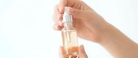 Female hand holding elegant glass perfume bottle with golden fragrance against clean white background for cosmetic and beauty product advertising.