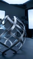 Modern spherical cage structure with metallic bands in contemporary studio setting with blue lighting and windows.