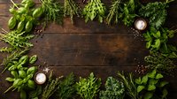Fresh green herbs and spices arranged as border frame on rustic wooden background with copy space for culinary design and cooking content.