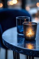Glowing candlelight in frosted glass holder on marble table creates cozy atmosphere with bokeh lights and blue tones, perfect for romantic evening ambiance.
