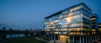 Modern glass office building illuminated at night with warm interior lighting against blue twilight sky in urban business district.